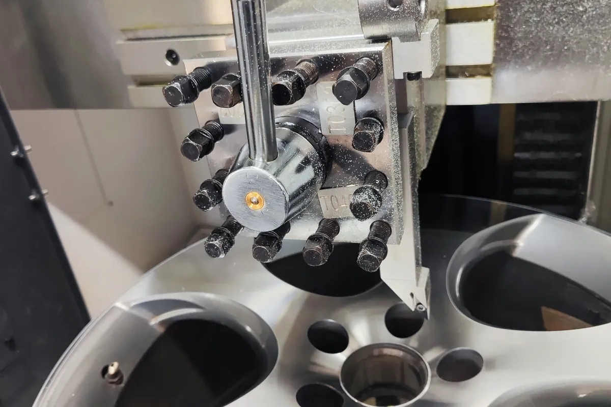 Głowica narzędziowa tokarki CNC ustawiona nad aluminiową felgą zamocowaną na wrzecionie