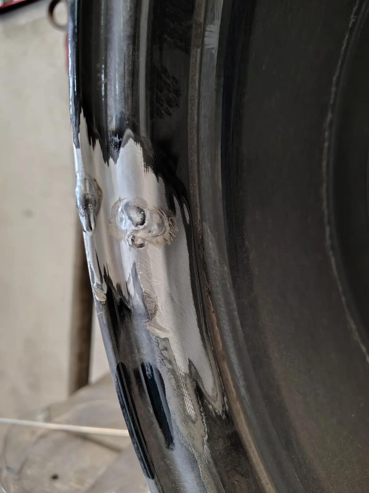 Naprawiany rant czarnej felgi aluminiowej z widocznym miejscem przygotowanym do obróbki